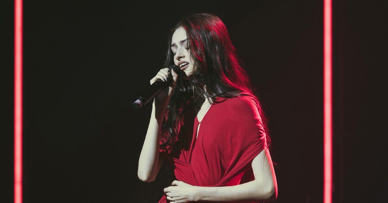 Solann en concert, micro en main, vêtue d'une robe rouge sous des projecteurs