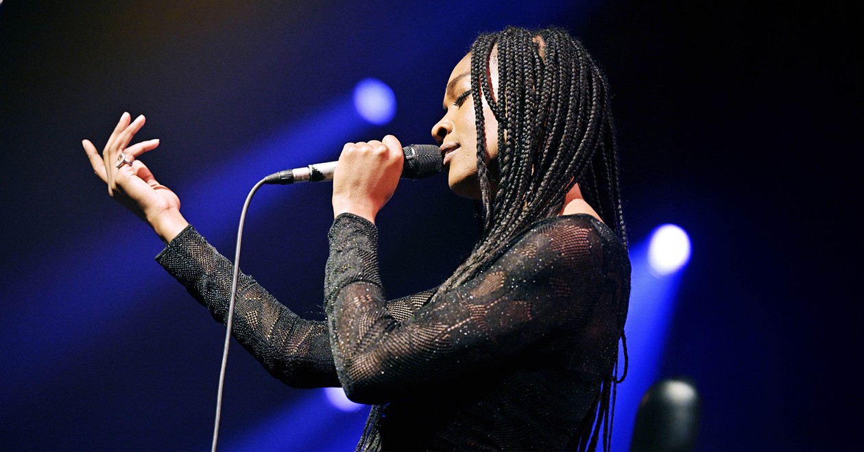Celia Kameni en concert, micro en main, sous les projecteurs bleus.