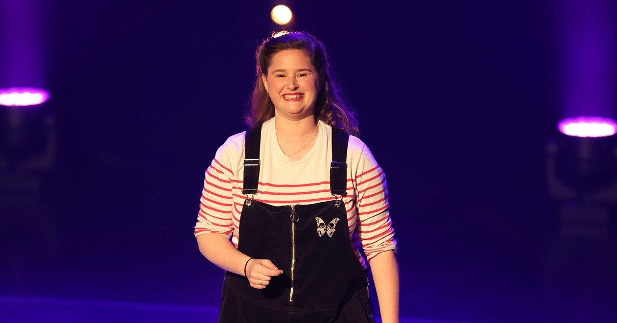 Élodie Poux sur scène, souriante, sous les projecteurs violets.