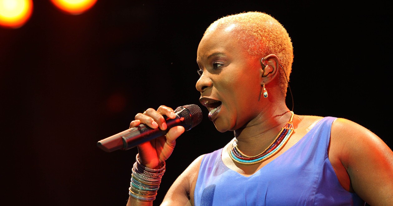 Angélique Kidjo performing live, holding a microphone, under stage lights