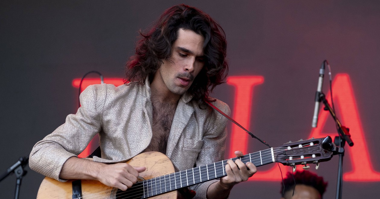 Zé Ibarra performing live, guitar in hand, under stage lights
